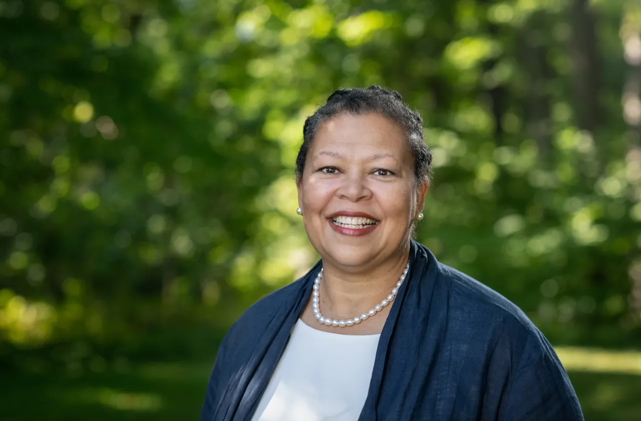 Photo of Sarah Willie-LeBreton smiling outdoors, in front of a background of green trees