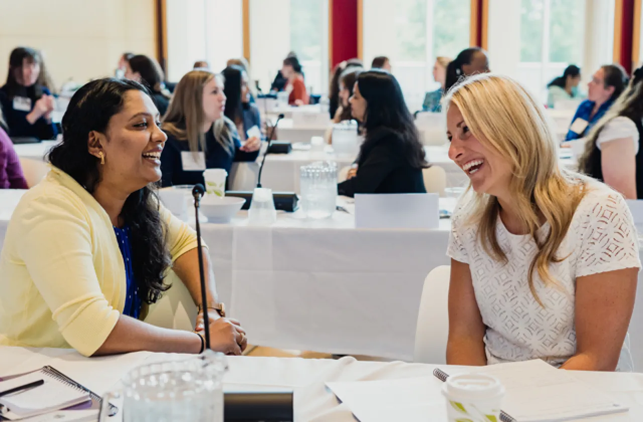 Two women laughing at a table during a conference.