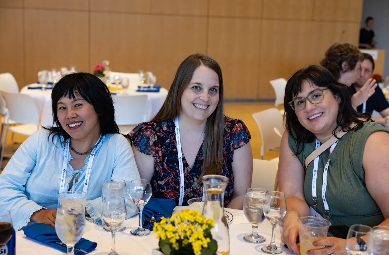 Three alums, seated together around a table, smile toward the camera