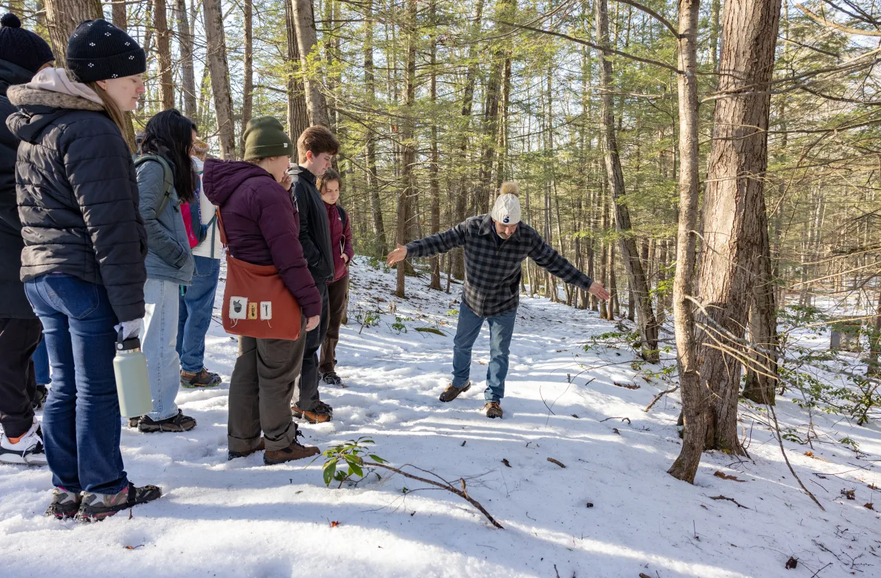 Smith's Outdoor Adventure Program manager Scott Johnson spreads his arms over the snow on a trail at MacLeish Field Station to show first-time animal trackers the size indicated by a print.