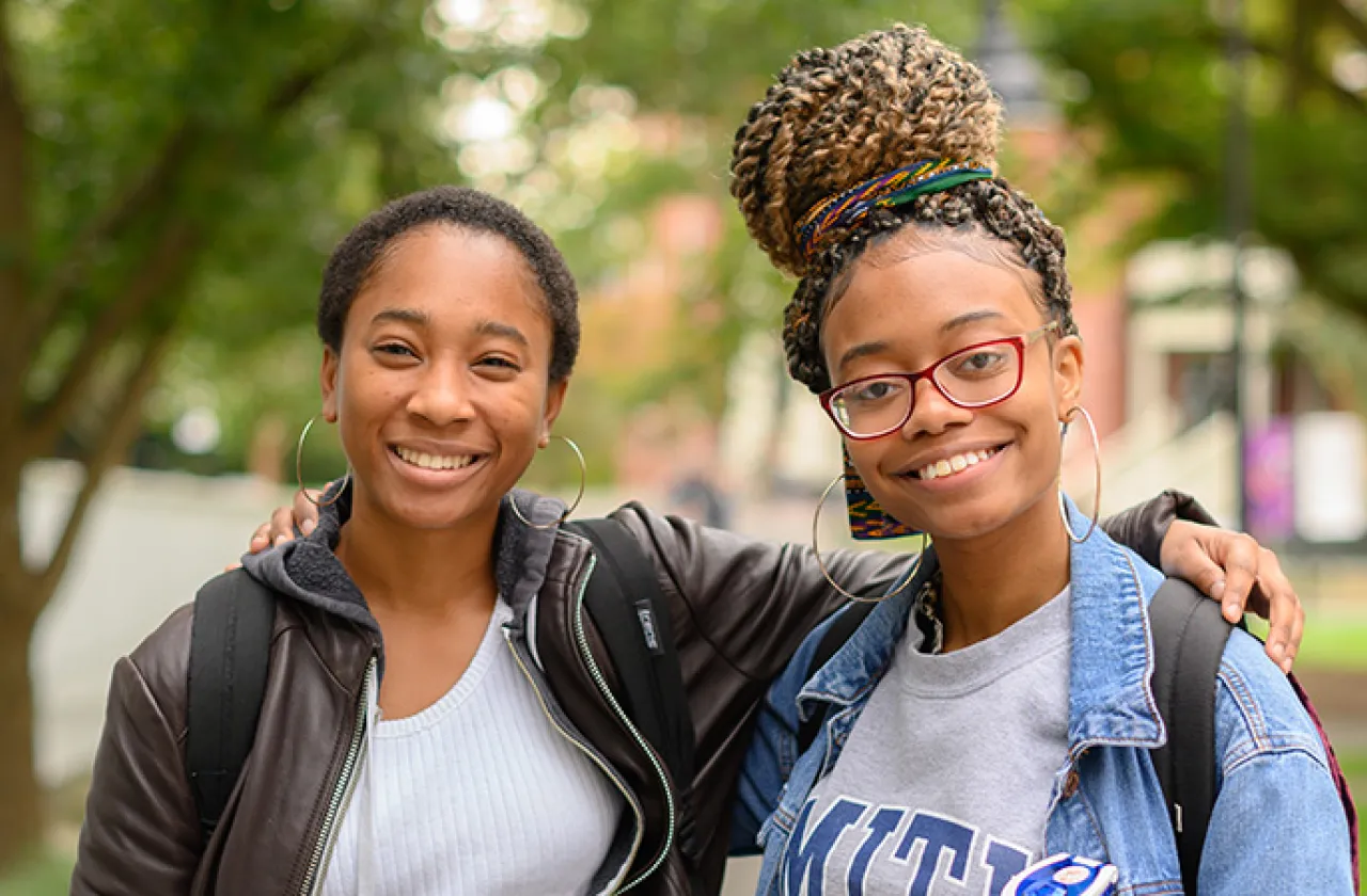Two students smiling, arms around each other's shoulders