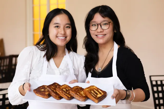 Two students smile holding a plate of food on IS Day