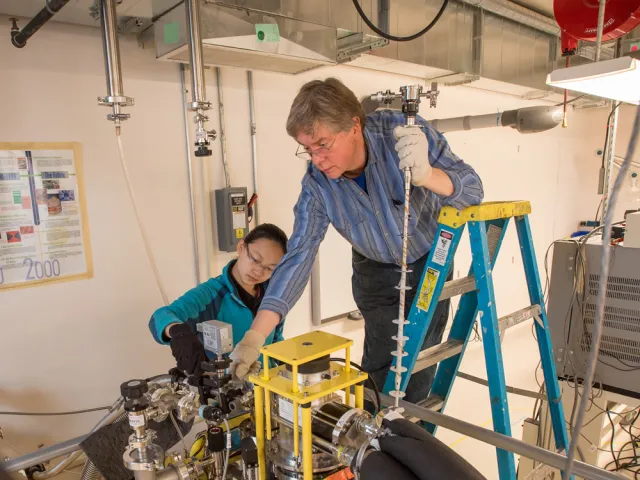 Nat Fortune leaning over a mechanical device with a student adjusting dials