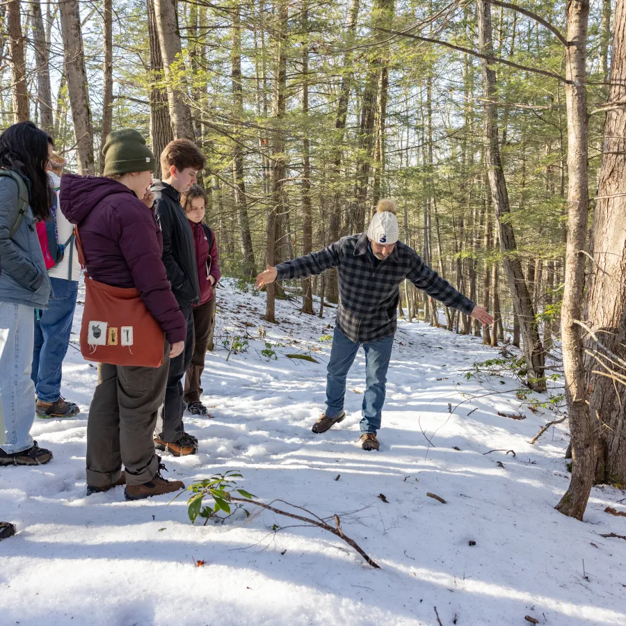 Smith's Outdoor Adventure Program manager Scott Johnson spreads his arms over the snow on a trail at MacLeish Field Station to show first-time animal trackers the size indicated by a print.