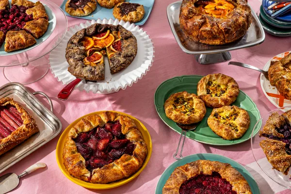 A collection of various galettes on colorful plates, all on a pink tablecloth.