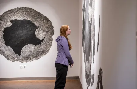 A student in the Smith Art Museum, staring intently at artwork on the right-hand wall