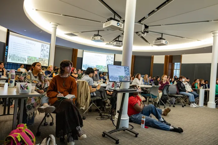 A wide shot of a classroom and many students sitting facing forward.