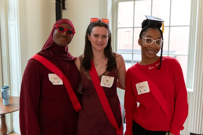 Three students wearing red sashes smile at the camera