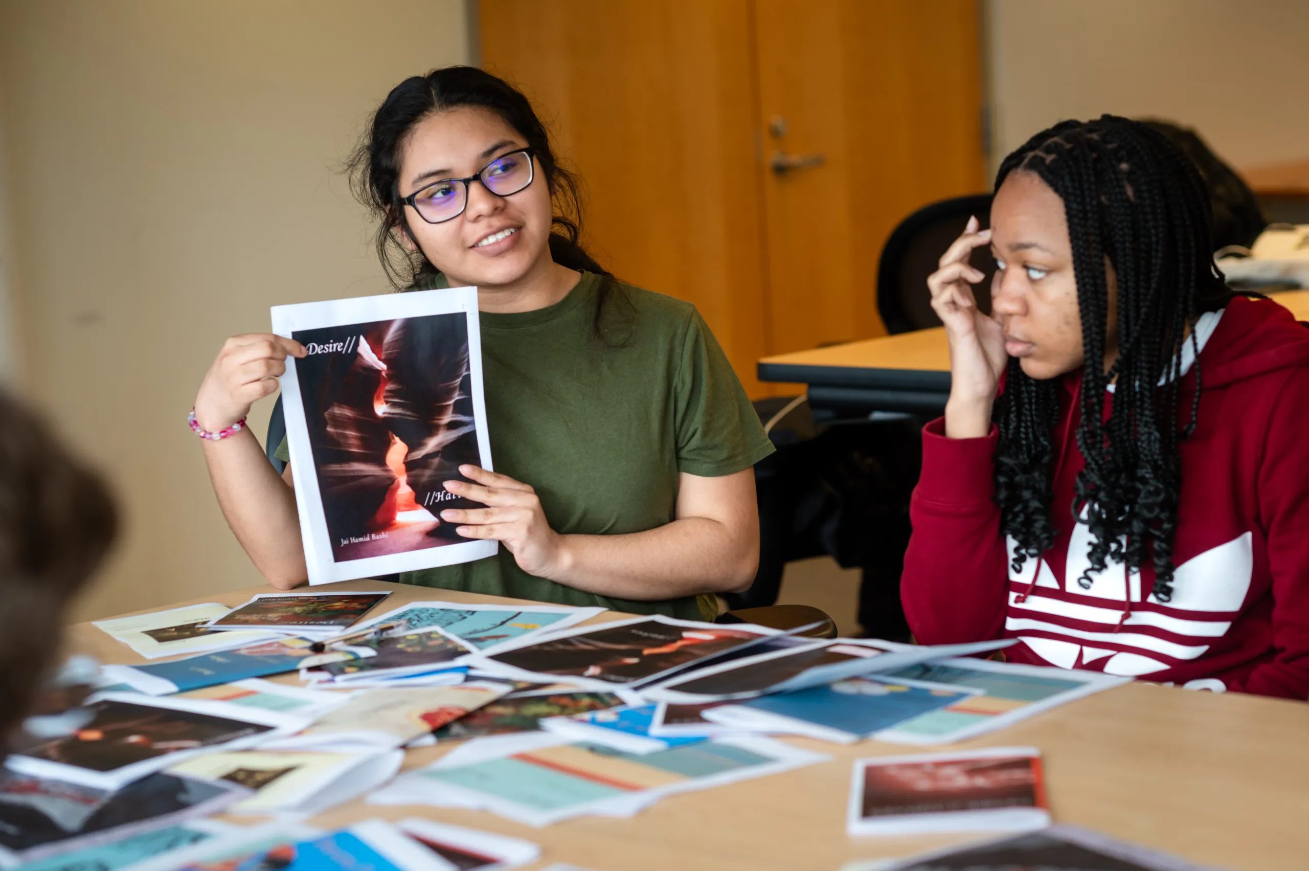A student holds up a photo of a chapbook cover