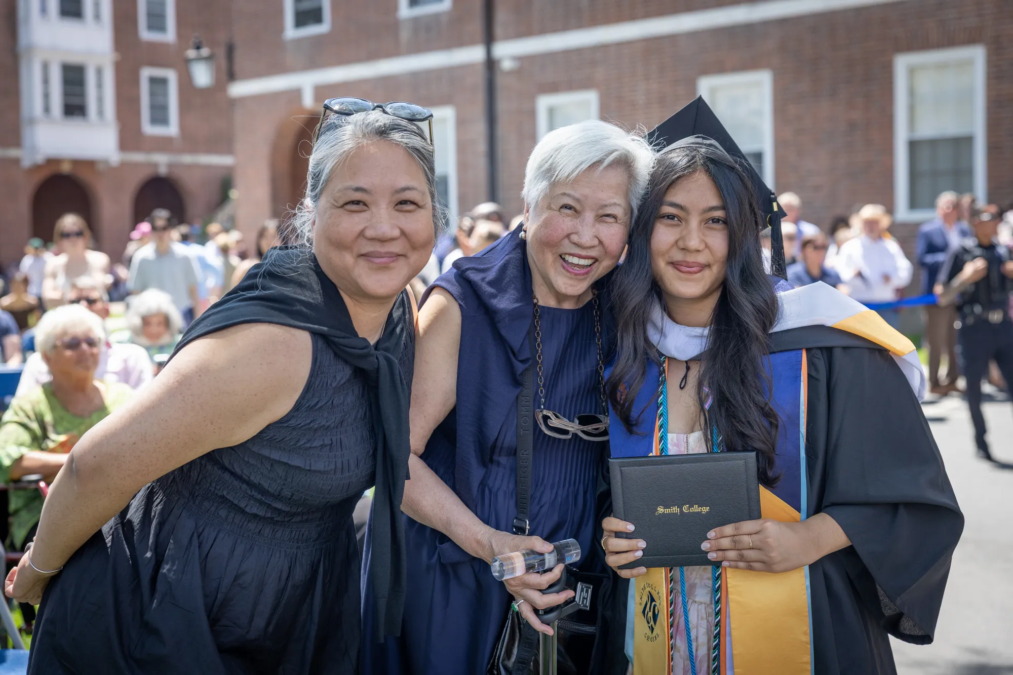 A student holds her diploma and smiles at the camera with family members.