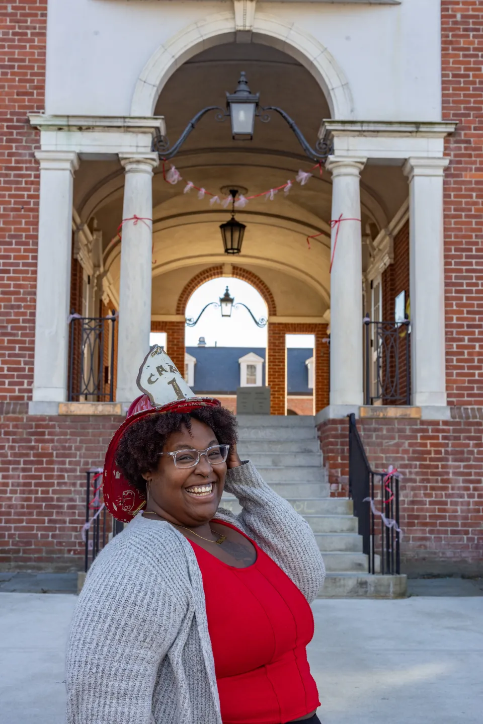 Diamond Jones stands outside of Comstock, smiling, wearing a red fire helmet and red top