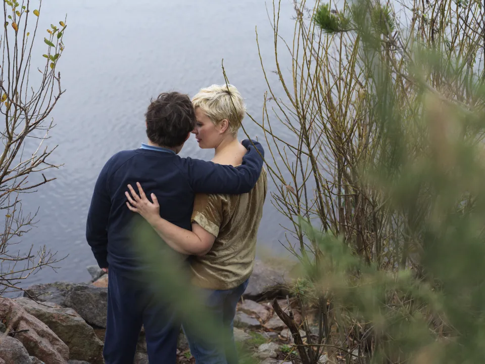 Cornwell stands with her arms around her son at the edge of a lake