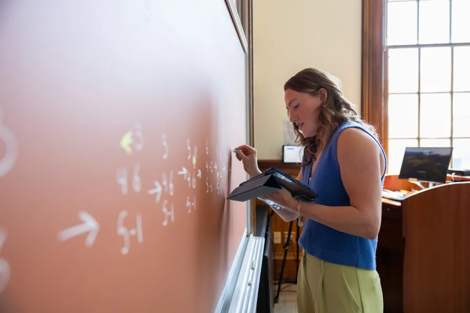 Kerry Seekamp writes on a tan-colored chalkboard.