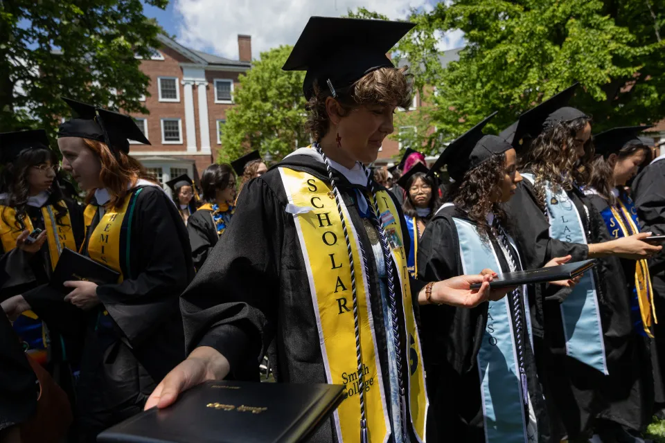 Students smile while passing diplomas in a circle after Commencement