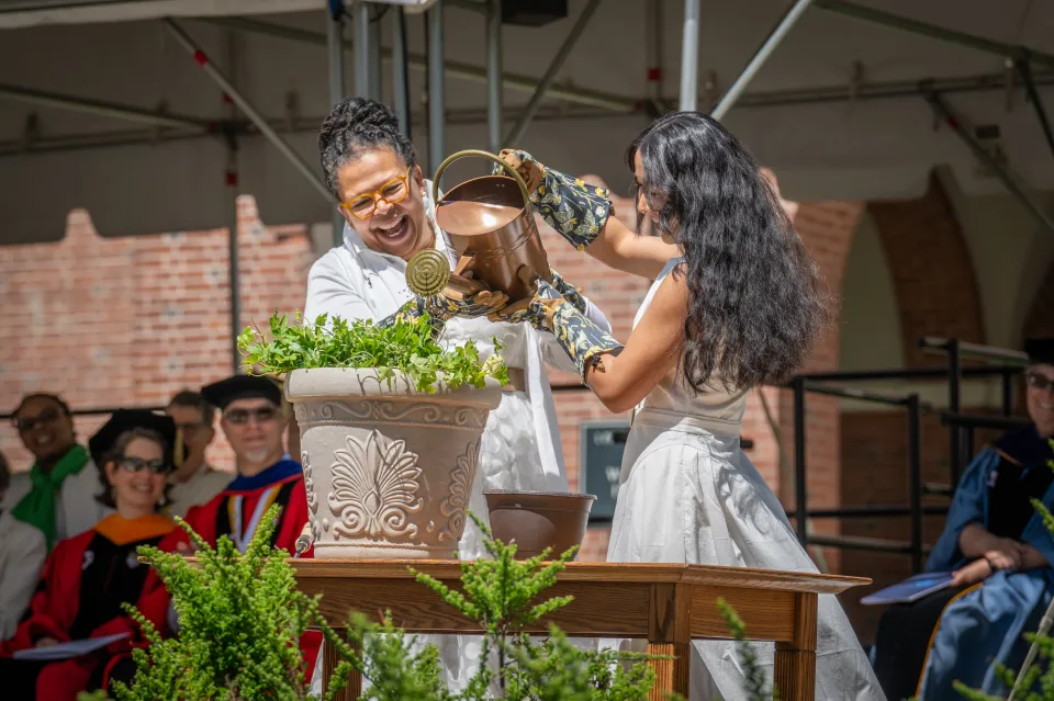 President Sarah Willie-LeBreton smiles while watering planted ivy with a student onstage during Ivy Day 2026.